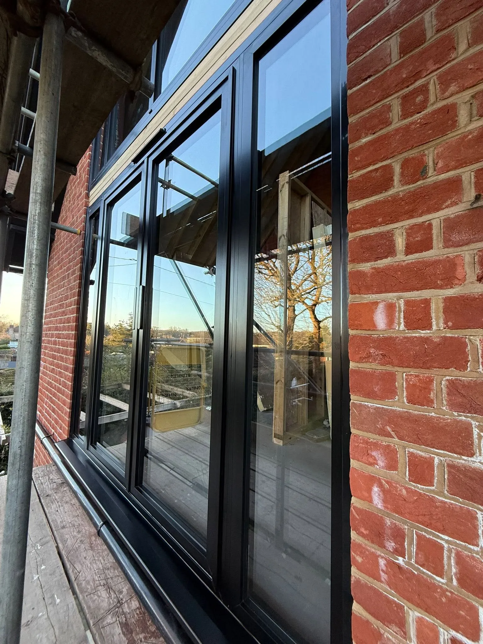 Close view along black aluminium door frames on the first floor, seen from the scaffolding