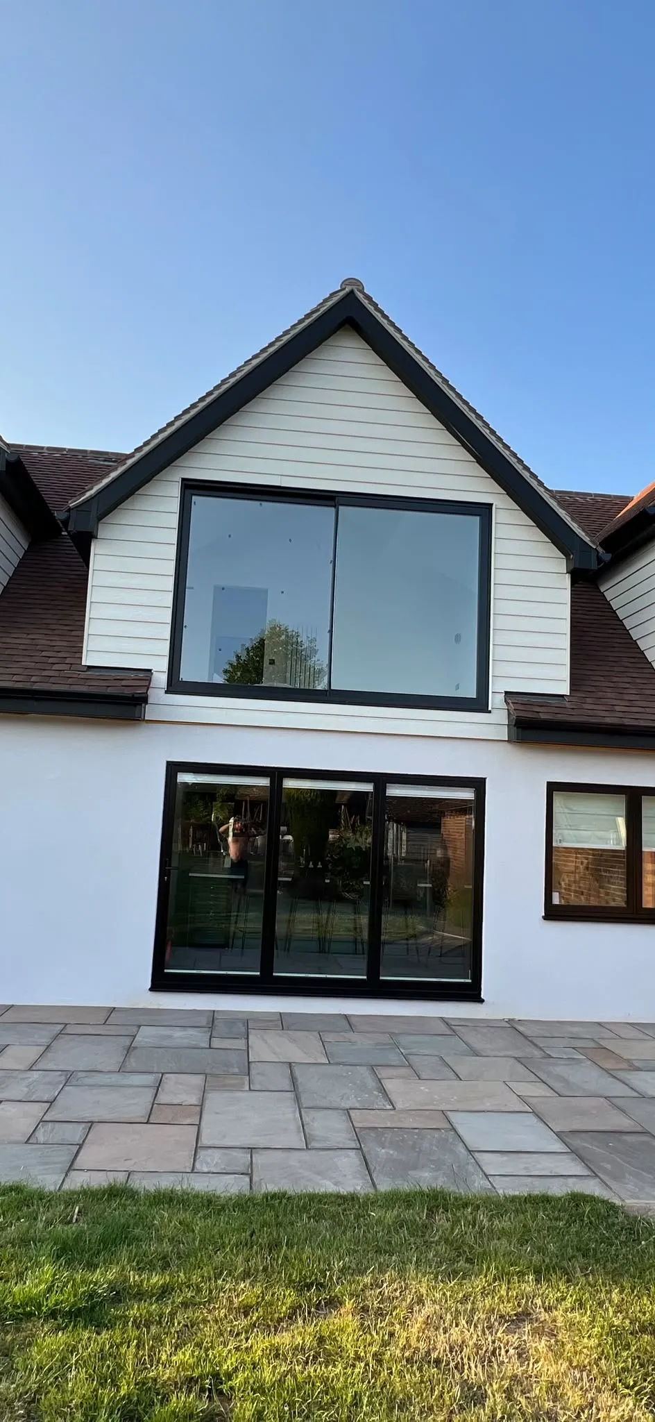 White rendered and weatherboarded home with a black aluminium gable window above black sliding doors