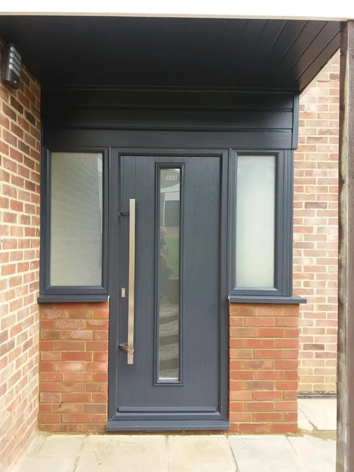 Anthracite composite front door with a full-height bar handle and a window either side, in a recessed porch