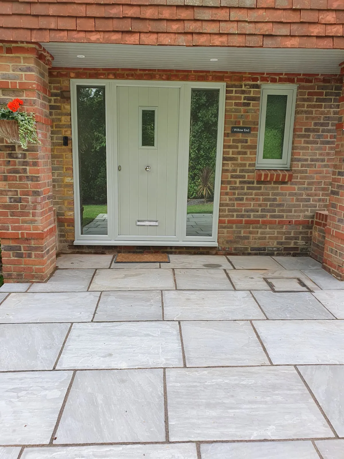 Pale sage composite front door with full-height glazed side panels in a recessed brick porch