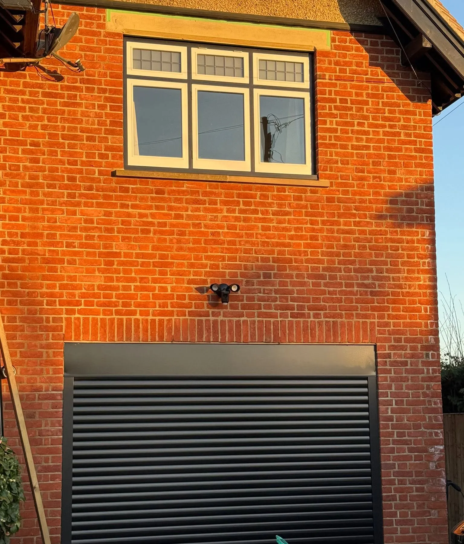 New dark electric roller garage door, with a timber window with leaded top-lights in the brickwork above