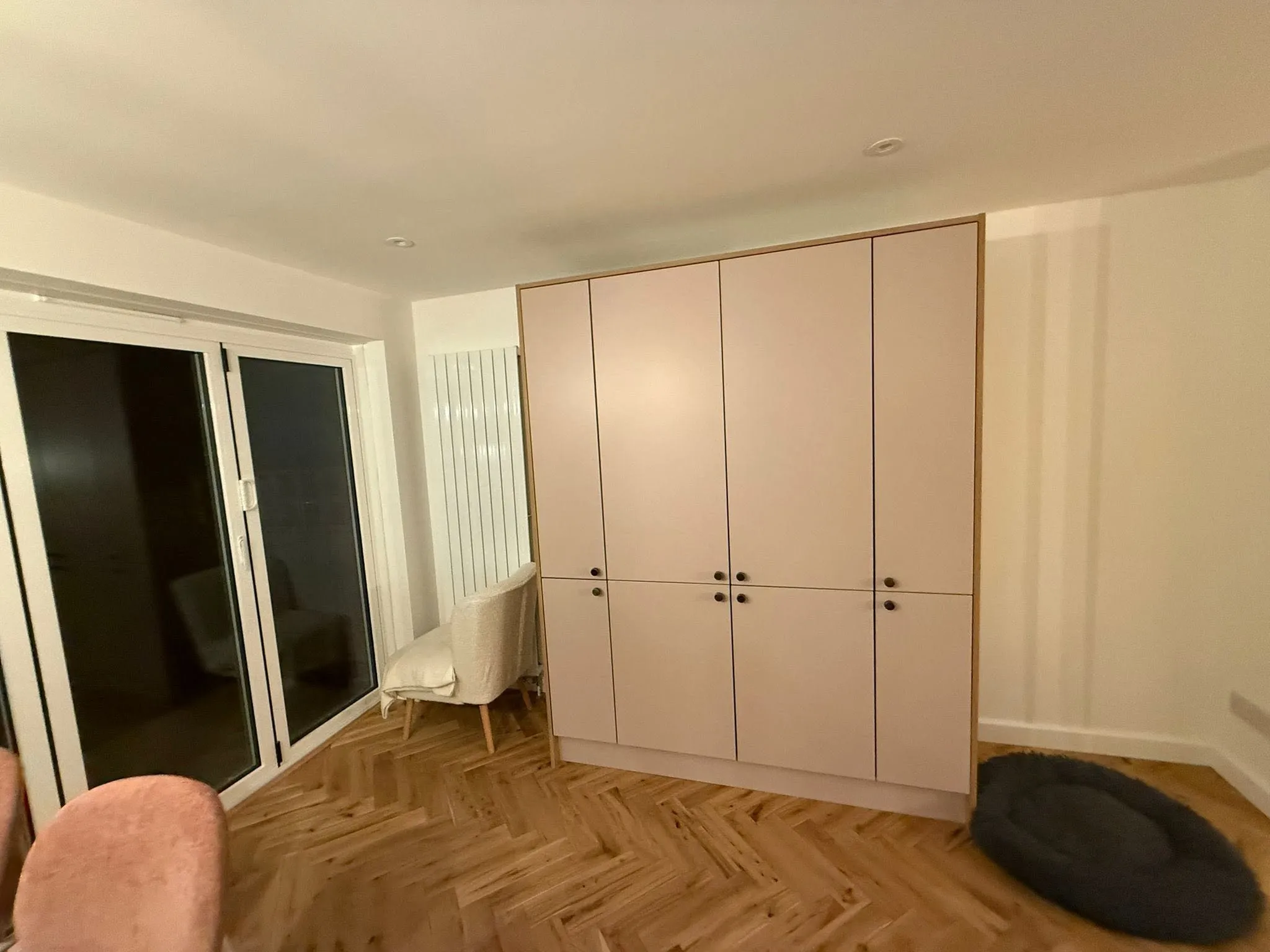 Fitted full-height storage cupboards beside white bifold doors, on a herringbone floor