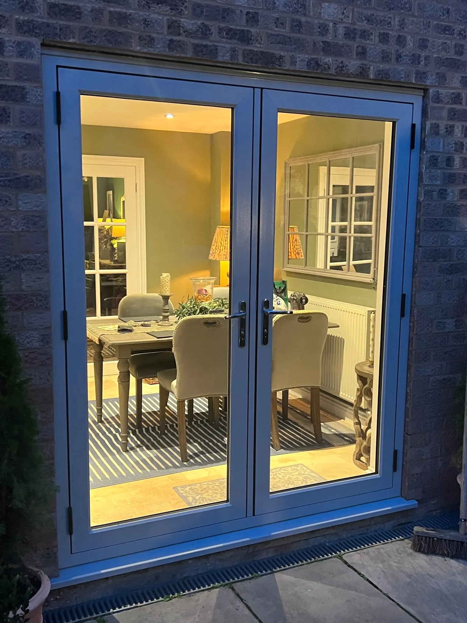 Blue-grey flush French doors at dusk, with a lit dining room behind