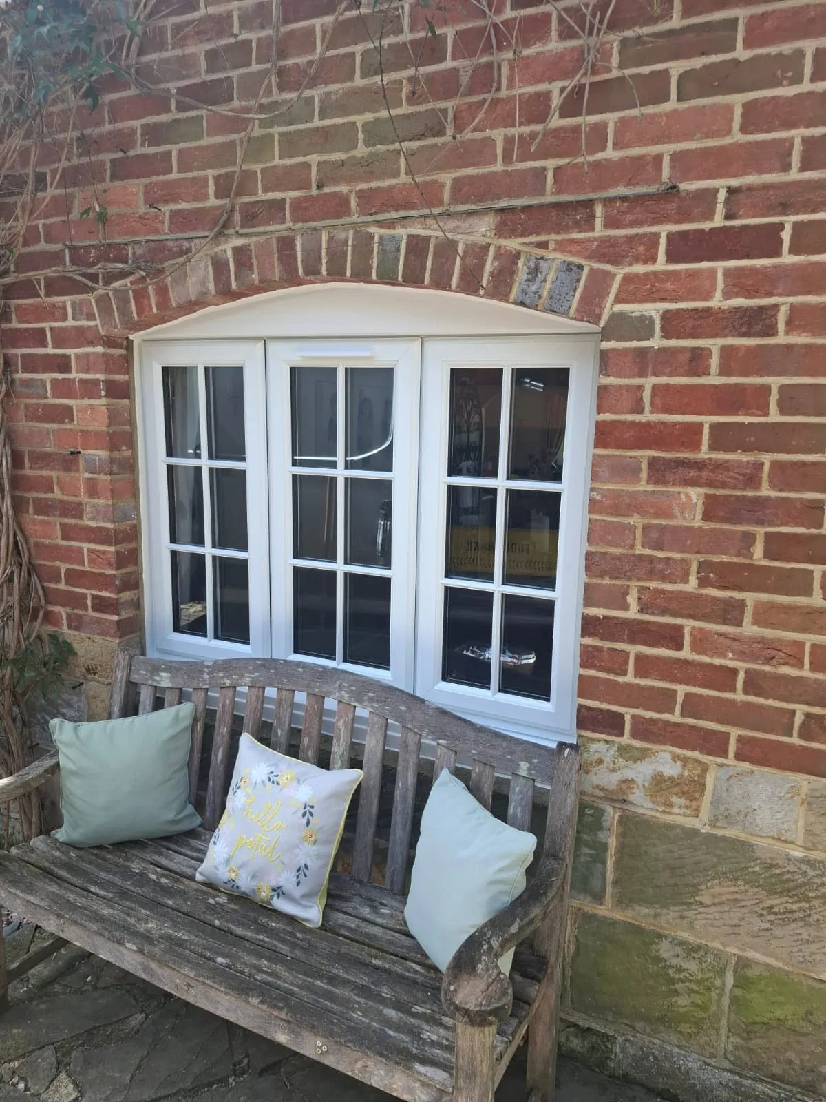 White window with Georgian bars in an arched brick opening, above a weathered garden bench