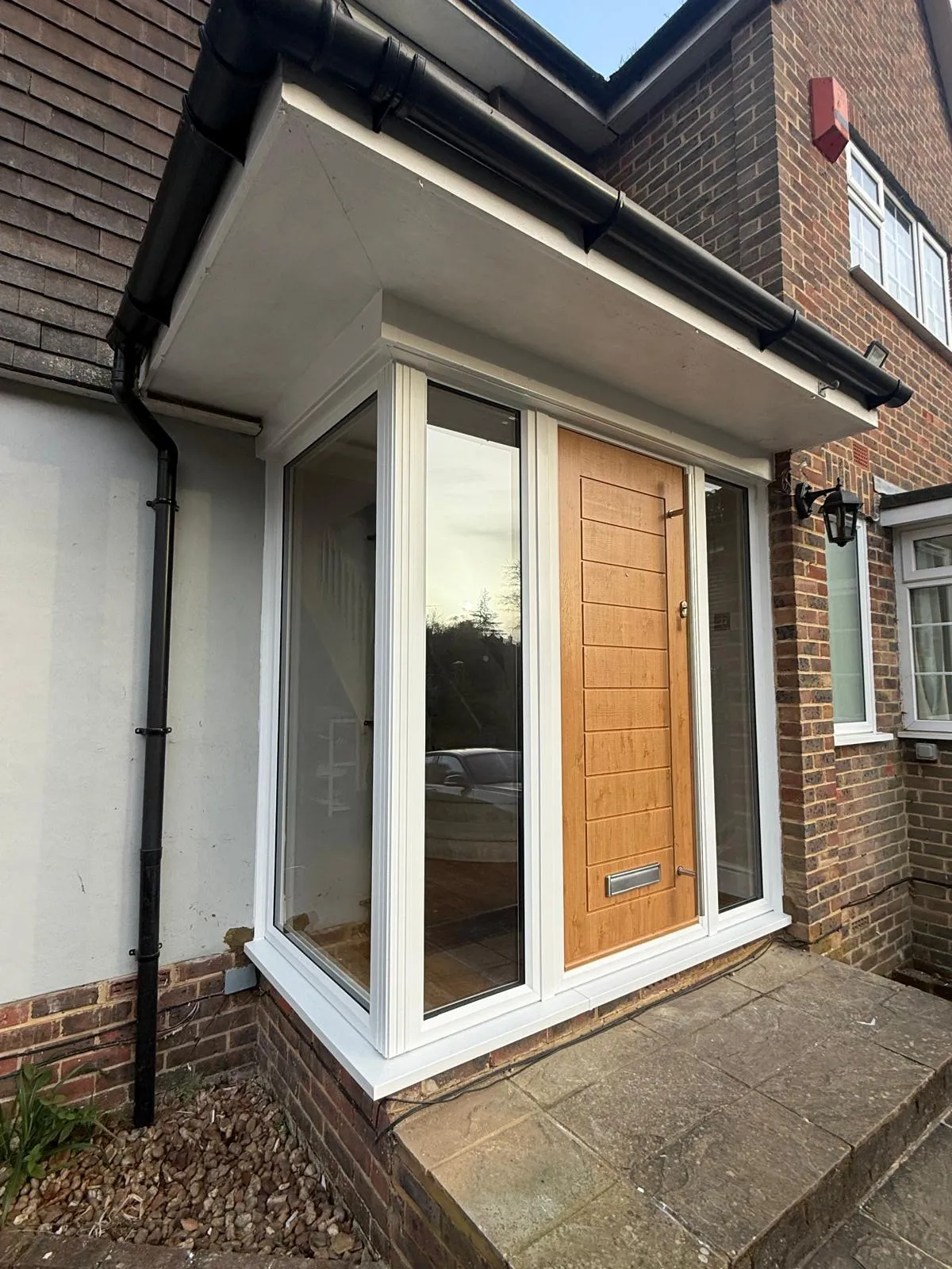 White glazed porch with an oak-effect composite door, beneath a flat canopy