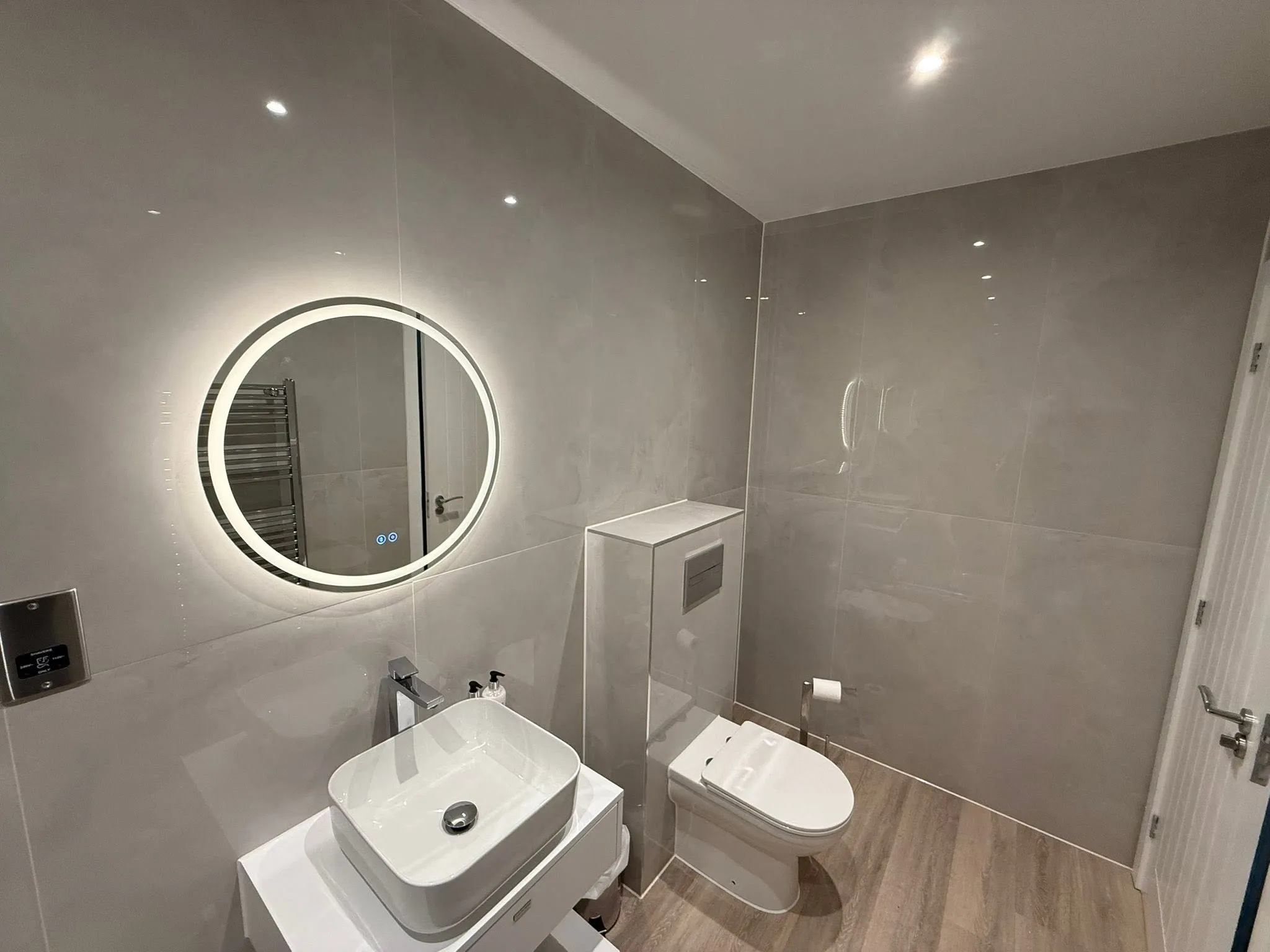 Round backlit mirror above a countertop basin and a back-to-wall WC