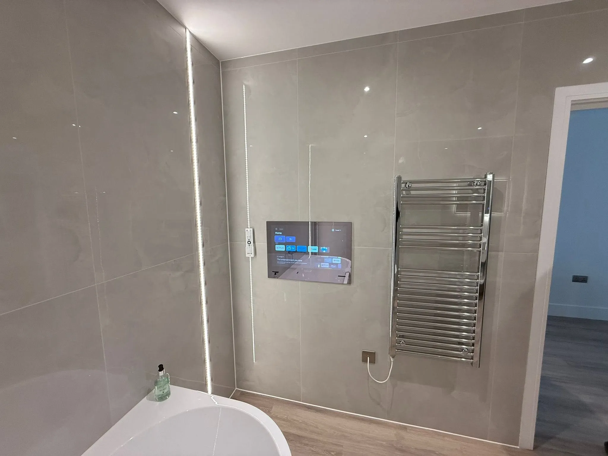 Bathroom wall with a built-in screen, a chrome heated towel rail and LED strip lighting