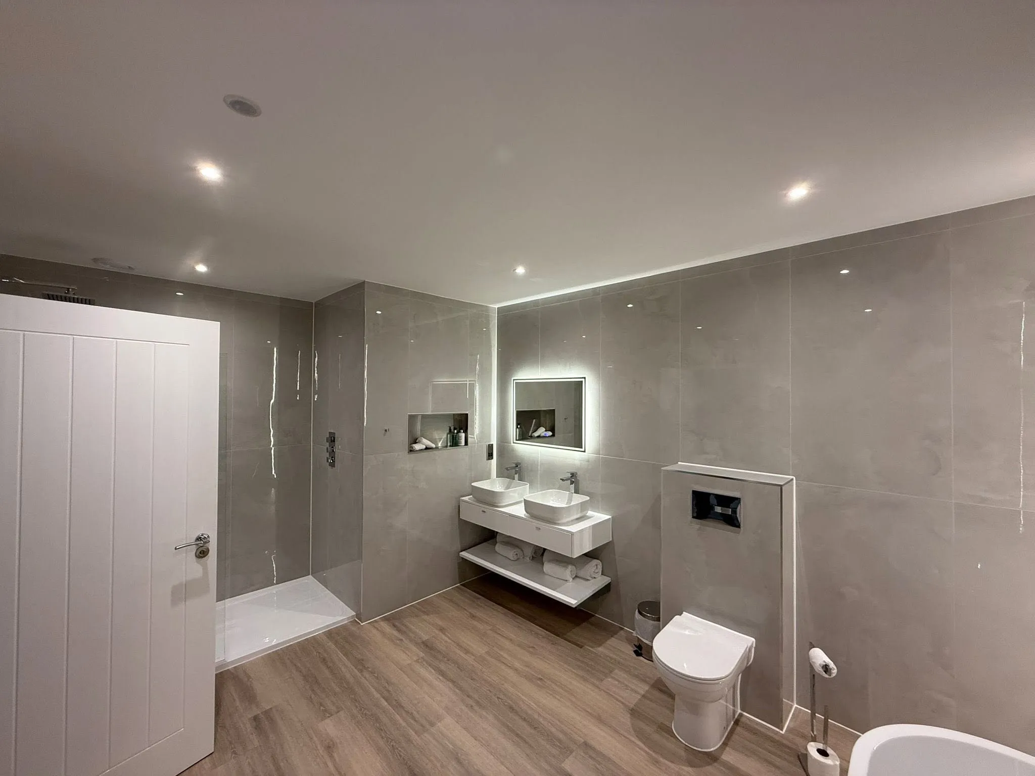 Suite bathroom with a walk-in shower, twin countertop basins, a backlit mirror and a wall-hung WC