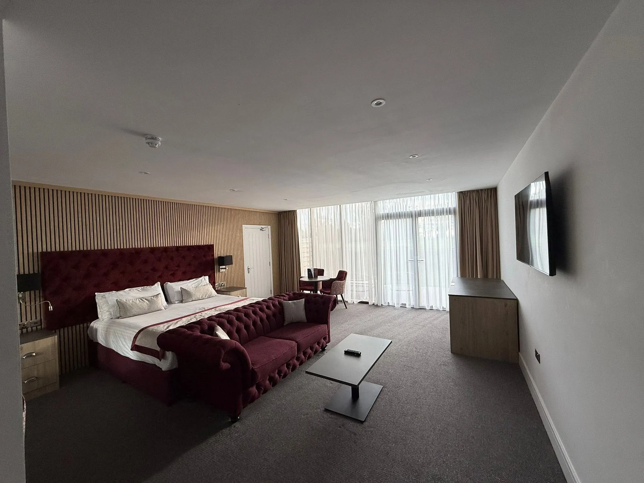 Second suite with a burgundy headboard and sofa, a slatted timber wall and full-height glazing