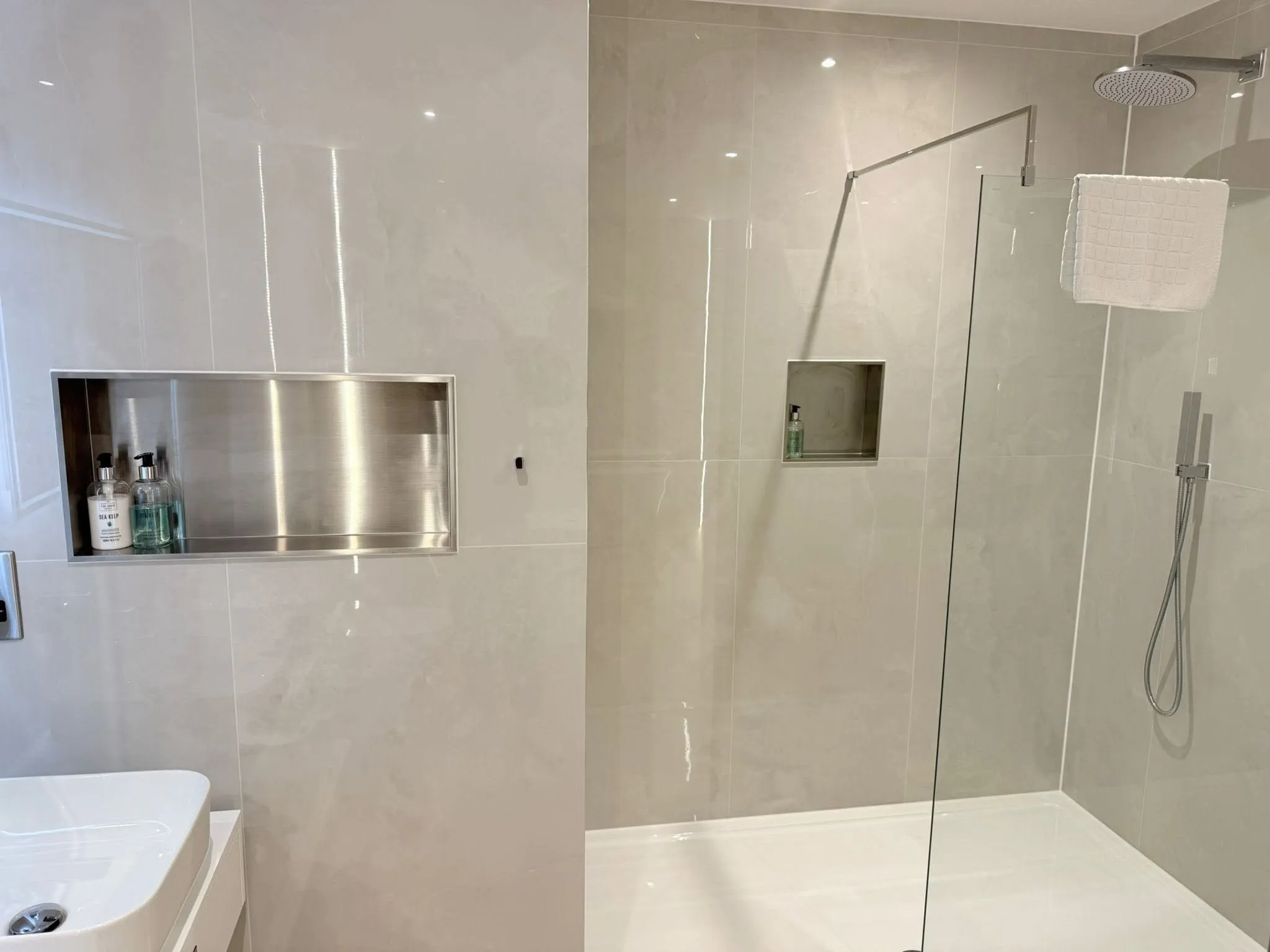 Walk-in shower with a frameless glass screen, a rainfall head and two recessed stainless steel niches