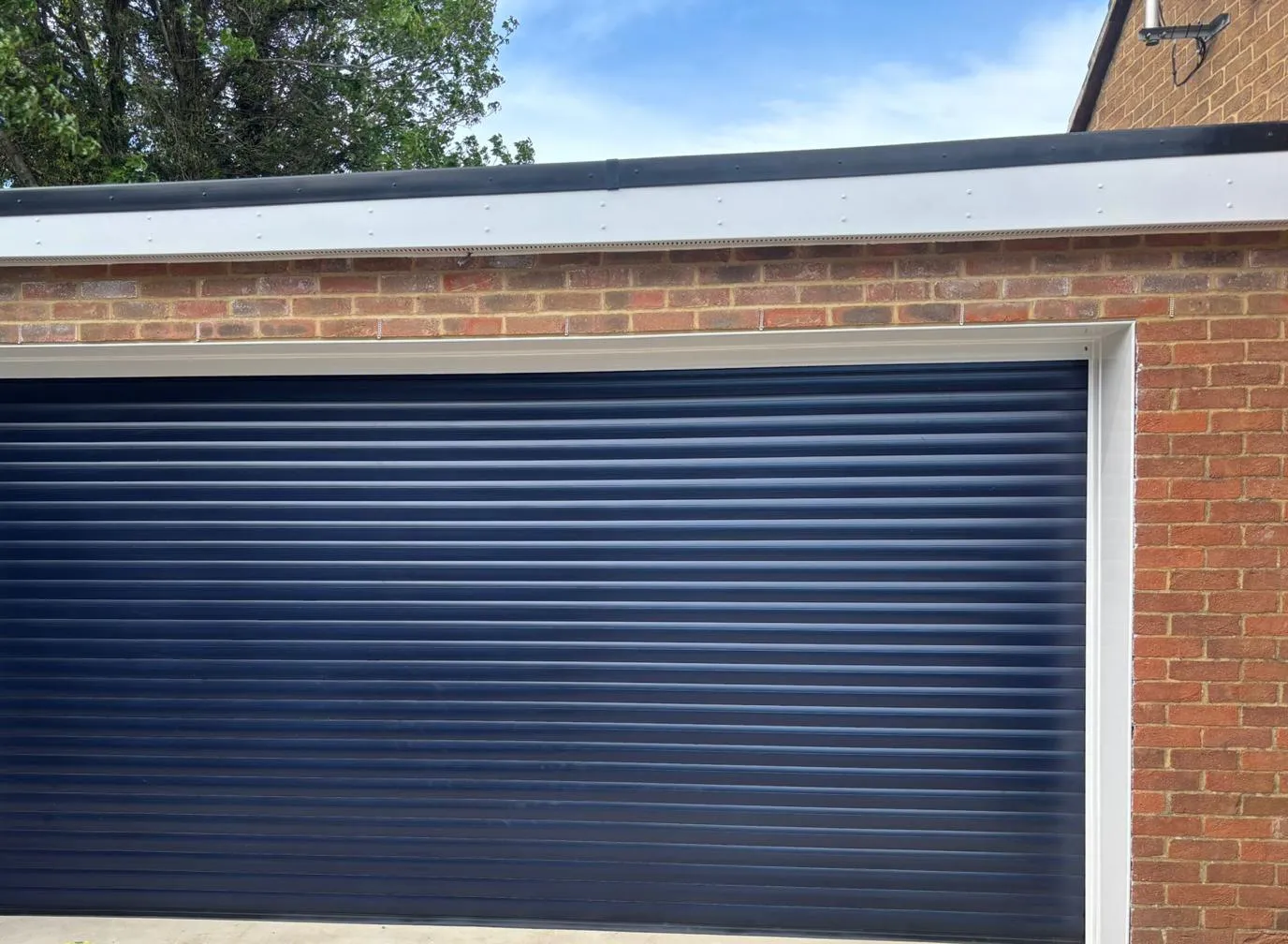 Navy electric roller garage door with a white surround in a brick garage