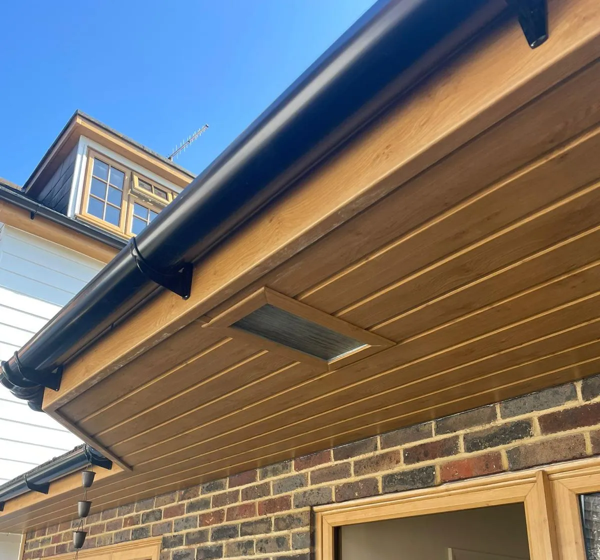 Oak-effect soffit and fascia with black guttering, above oak-effect window and door frames