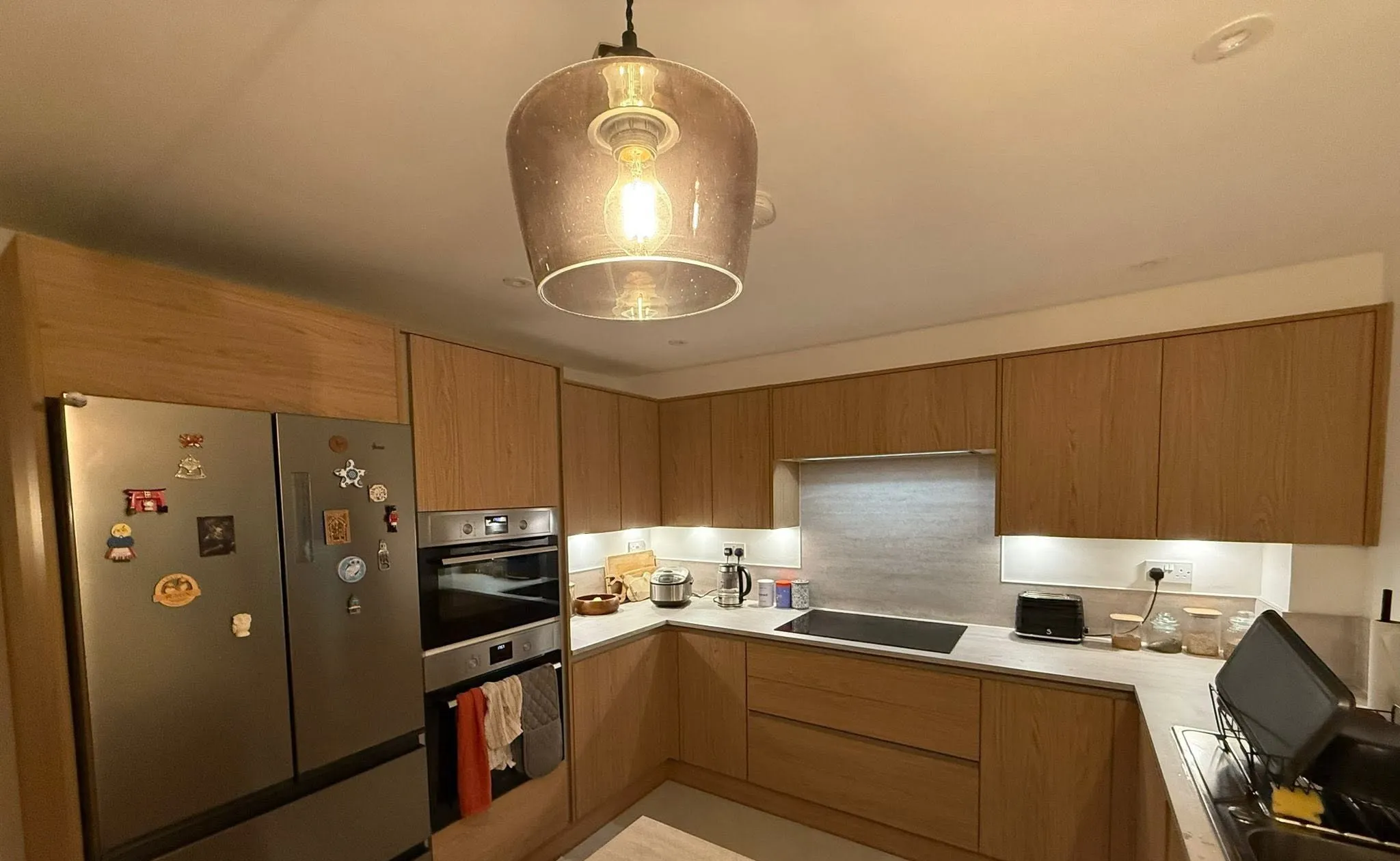 Oak-effect fitted kitchen with built-in ovens, an induction hob and under-cabinet lighting