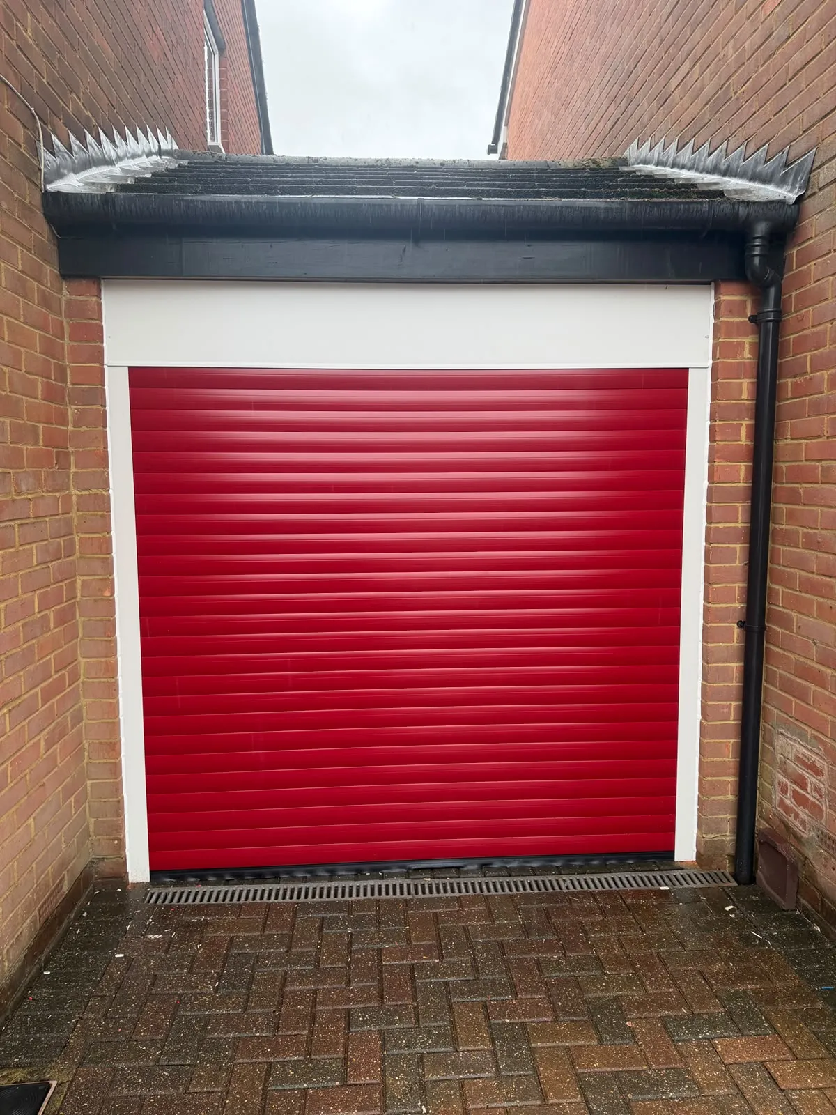 Red roller garage door with a white surround beneath new black fascia and guttering