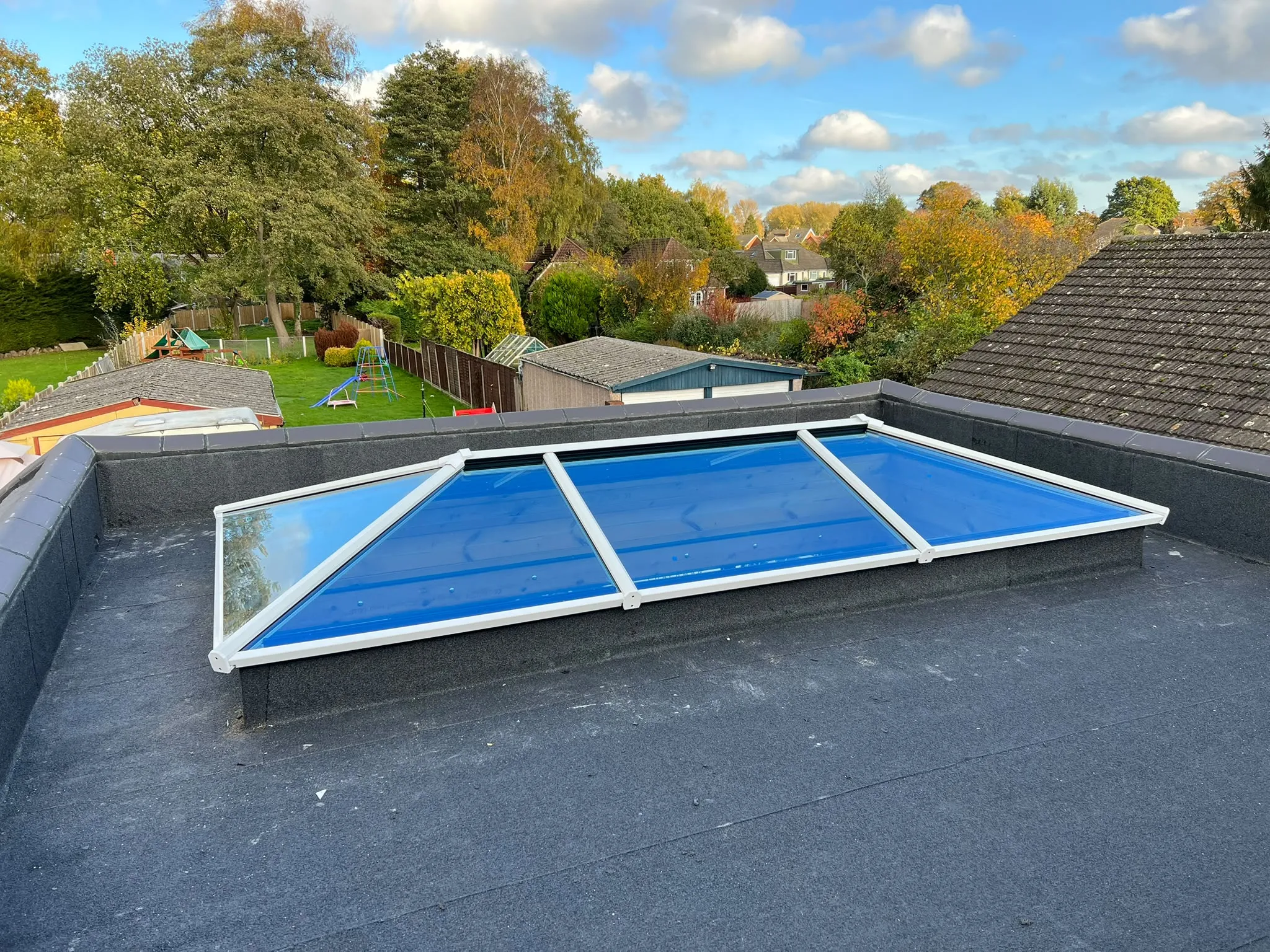 White-framed glass roof lantern on a flat roof, overlooking gardens