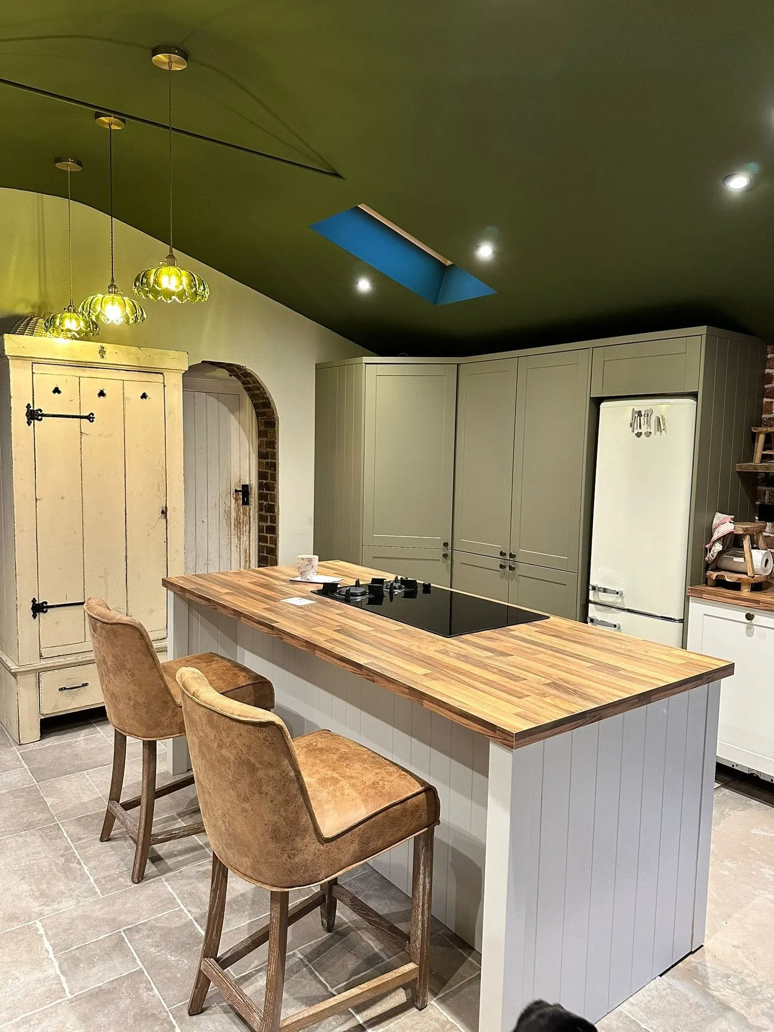 Sage green fitted kitchen with a large island and bar stools