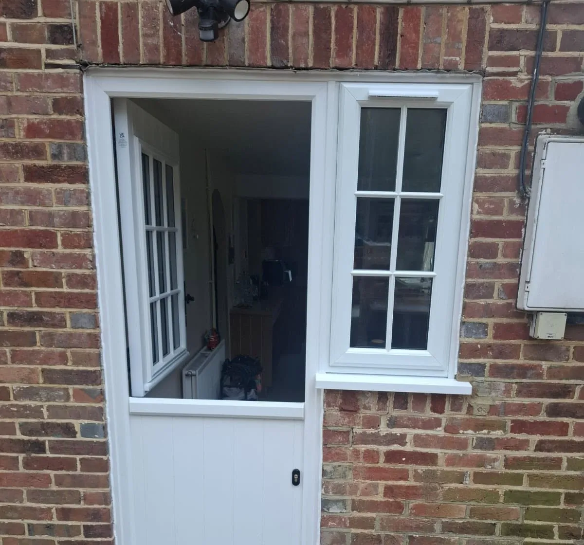 White stable door with its top half open, beside a matching window with Georgian bars