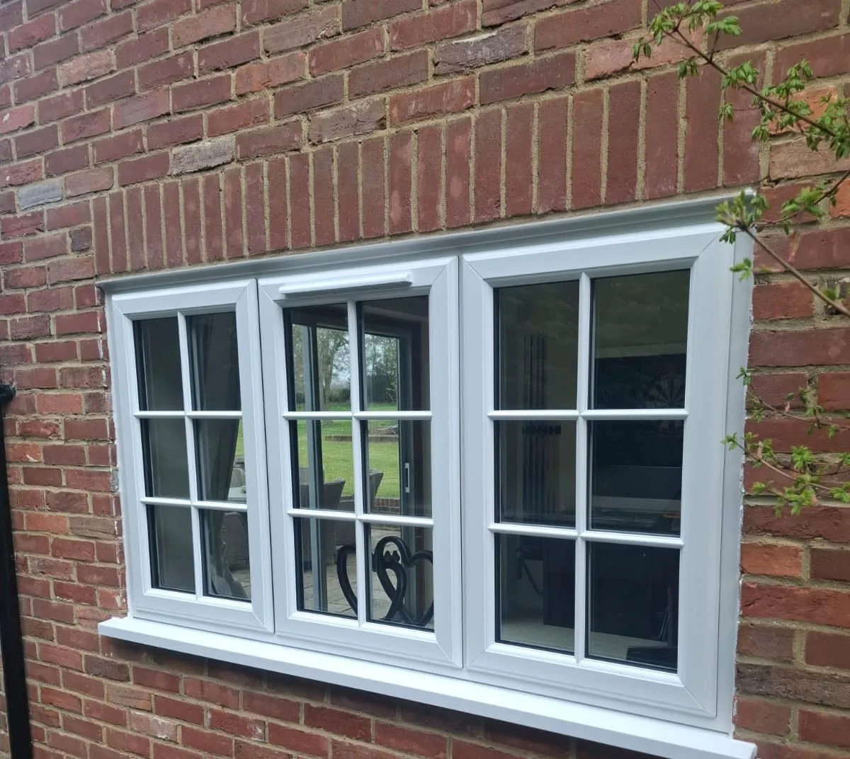 Three-light white casement window with Georgian bars, set in red brickwork