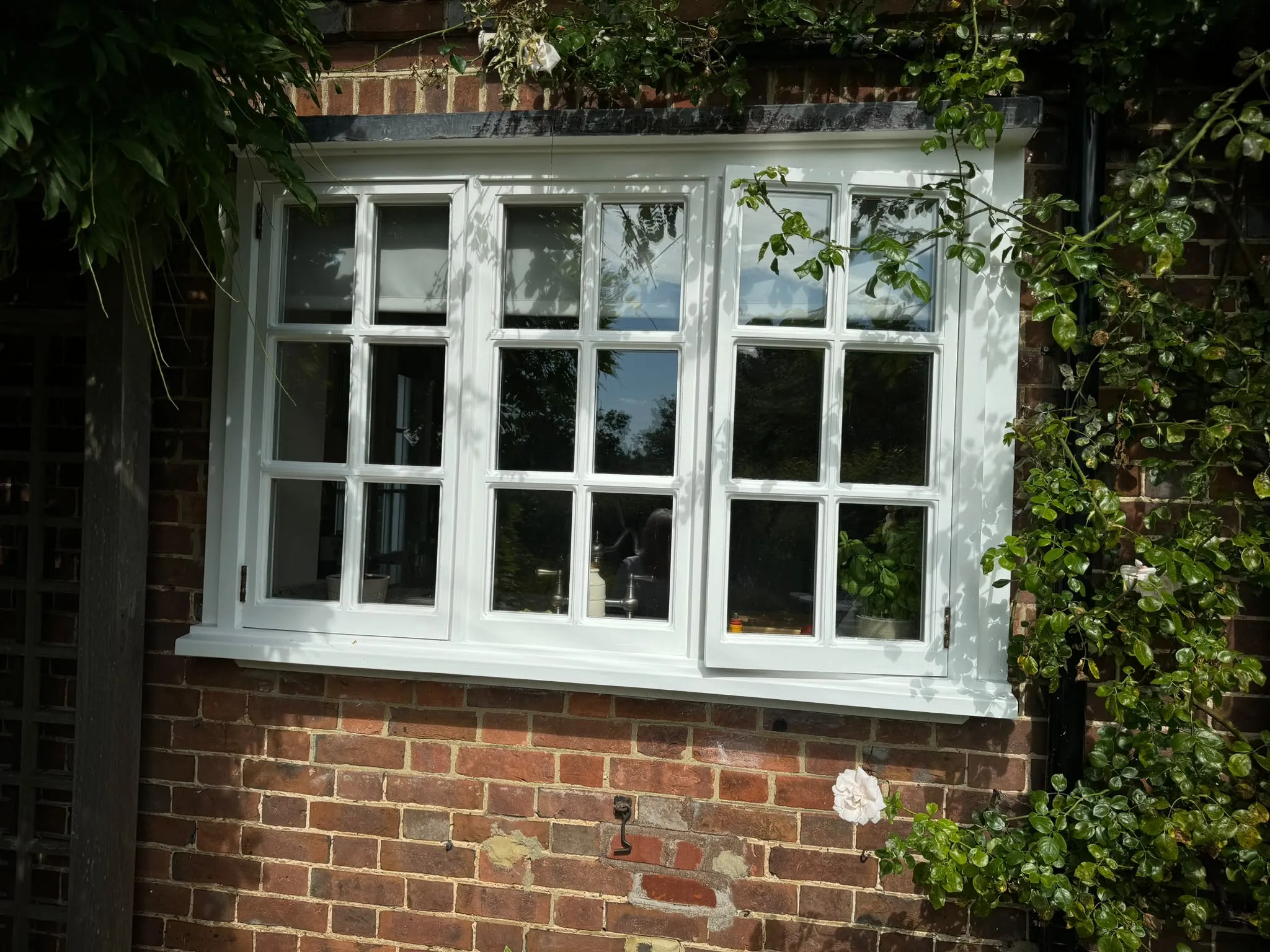 White timber casement window with Georgian glazing bars in a red brick wall, framed by climbing roses