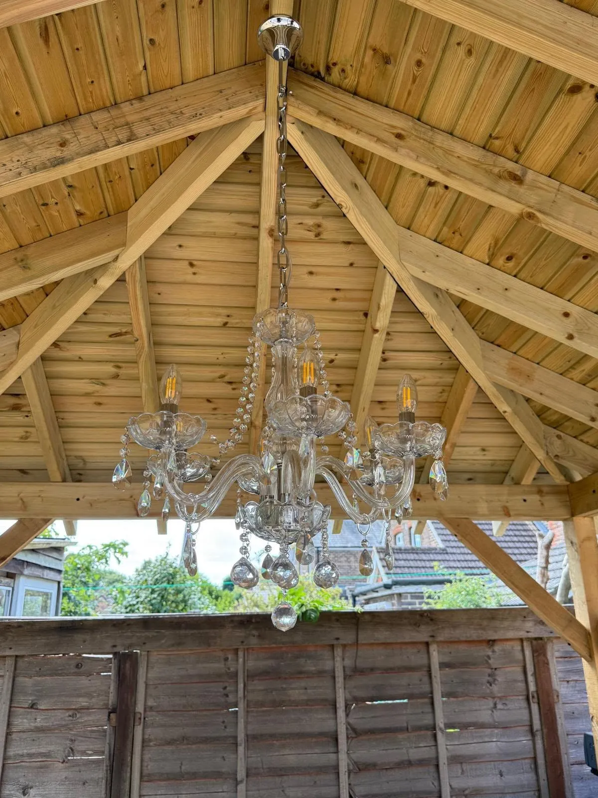 Chandelier hanging from the boarded ceiling of the timber pergola