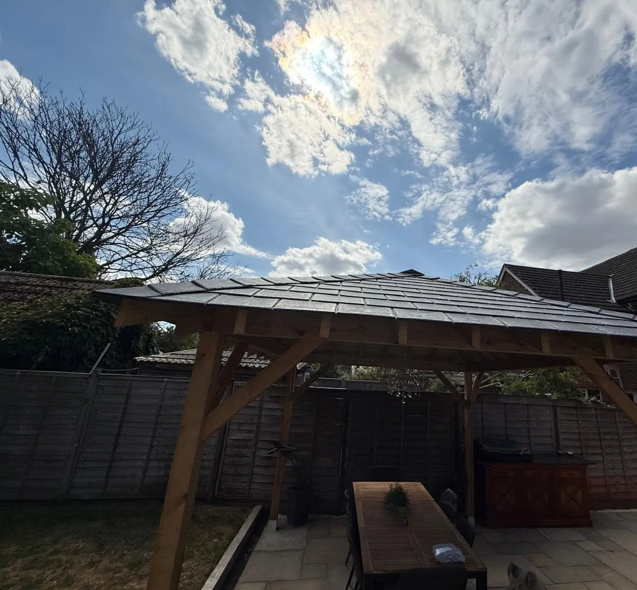 Timber-framed garden pergola with a hipped slate roof, against the sky
