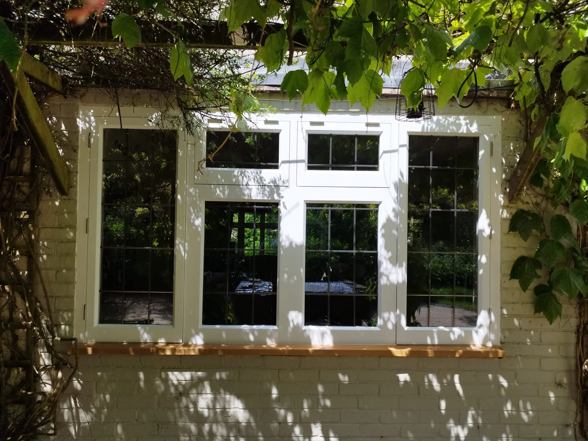 White timber window with leaded lights and an oak cill in a painted brick wall
