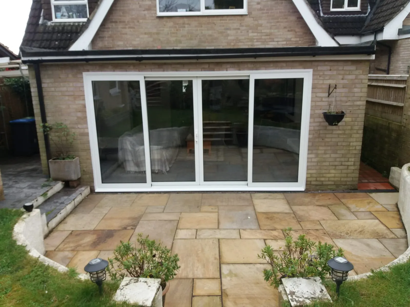 White aluminium sliding patio doors on a brick gable, opening onto a sandstone patio