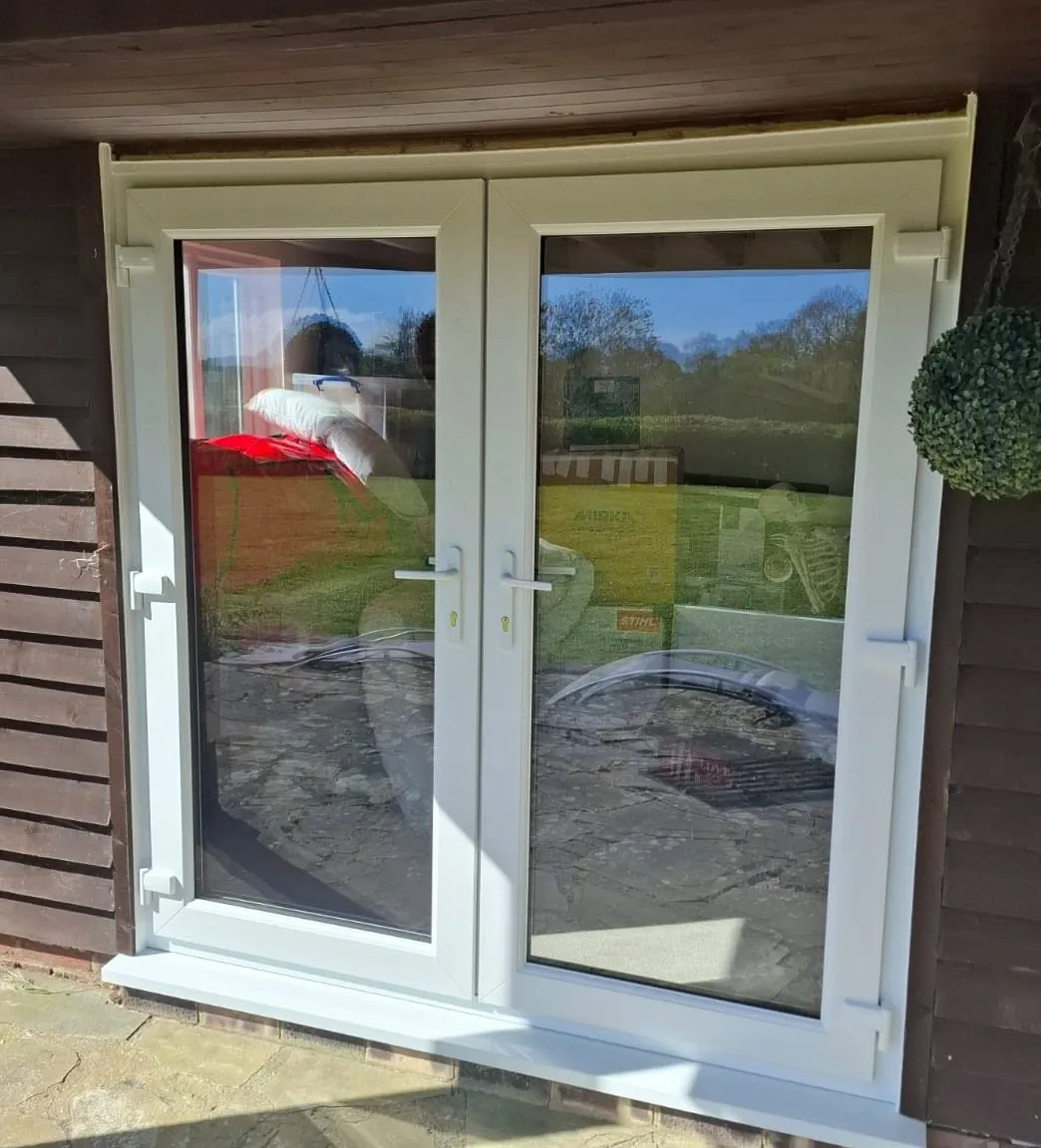Pair of white French doors in a dark weatherboarded building, reflecting the garden