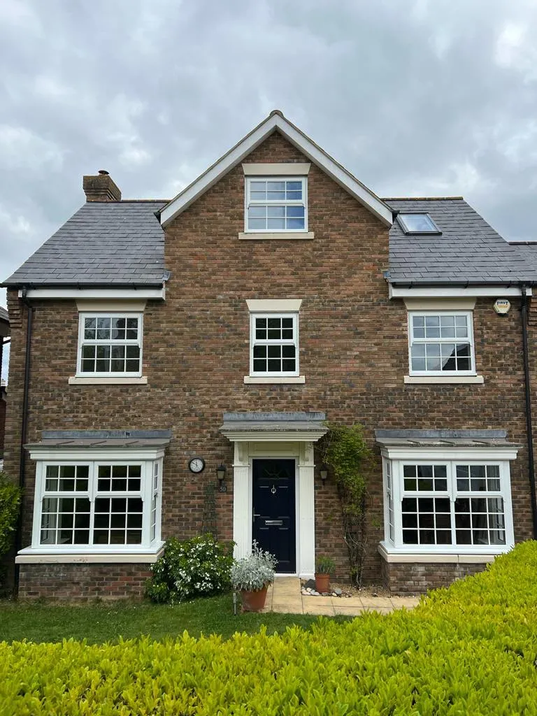 Three-storey brick townhouse with white sash windows with Georgian bars and a navy front door