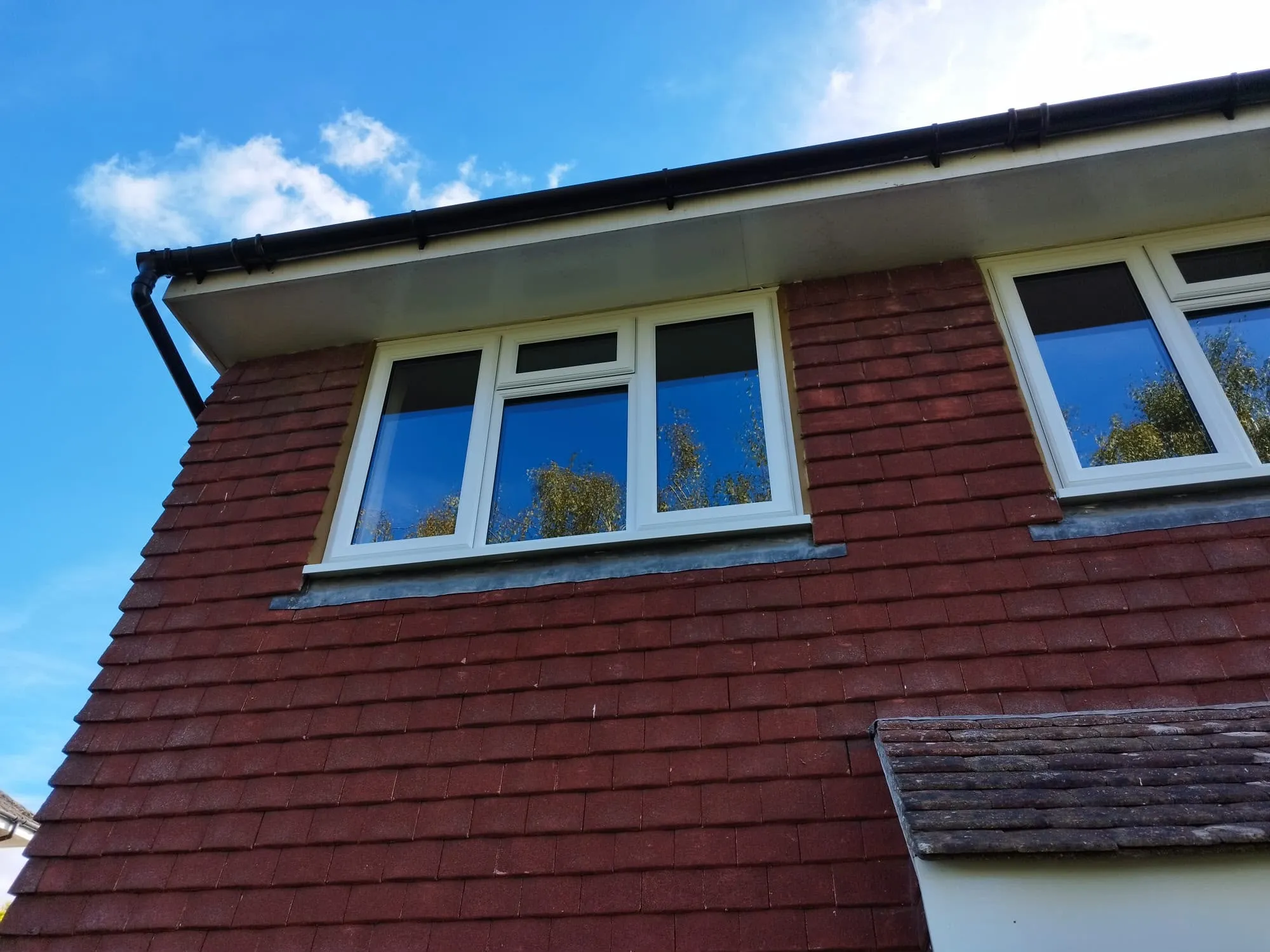 White soffit and fascia with black guttering above white windows in a tile-hung wall