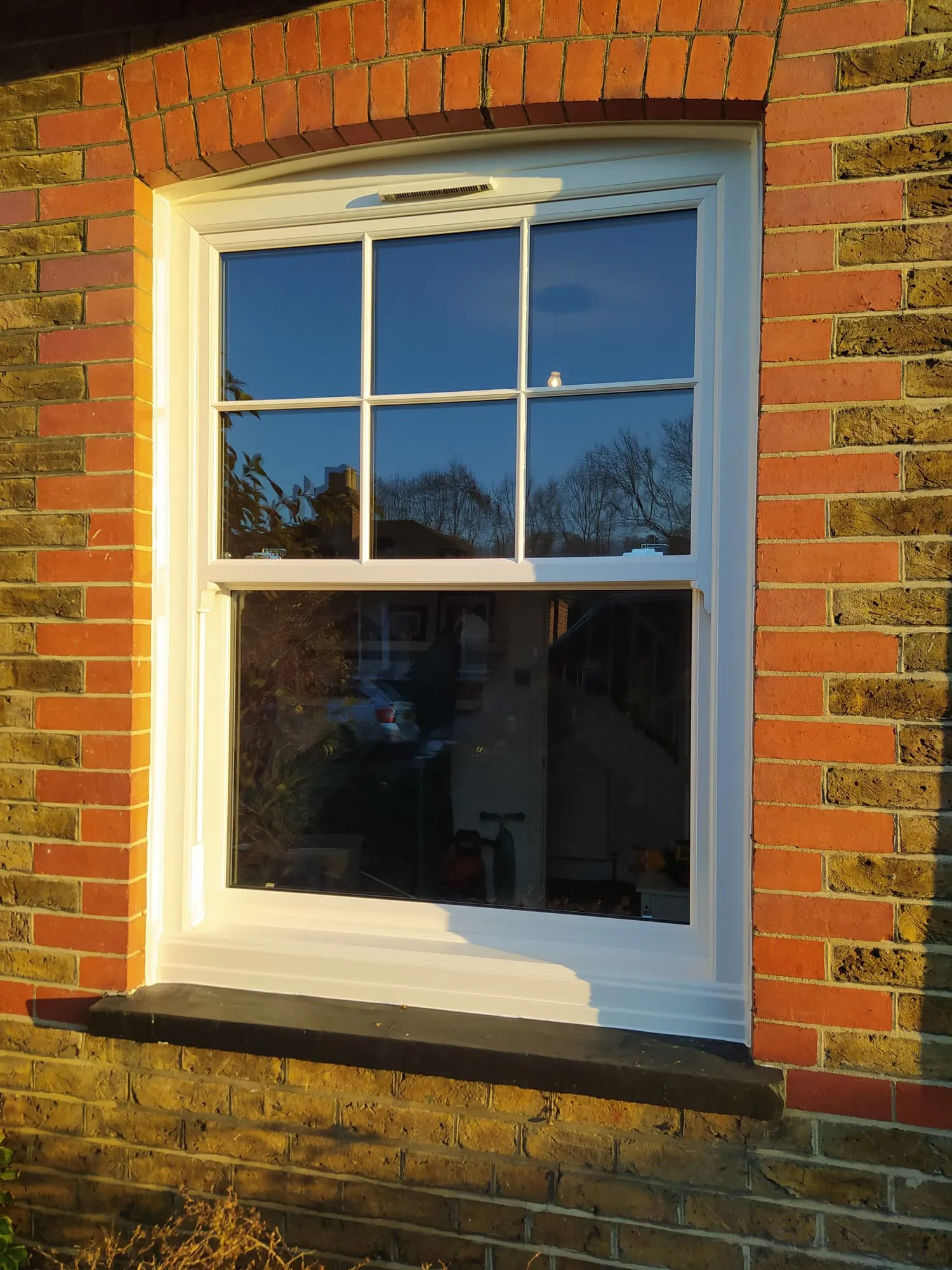 White uPVC sliding sash window with Georgian bars in an arched brick opening
